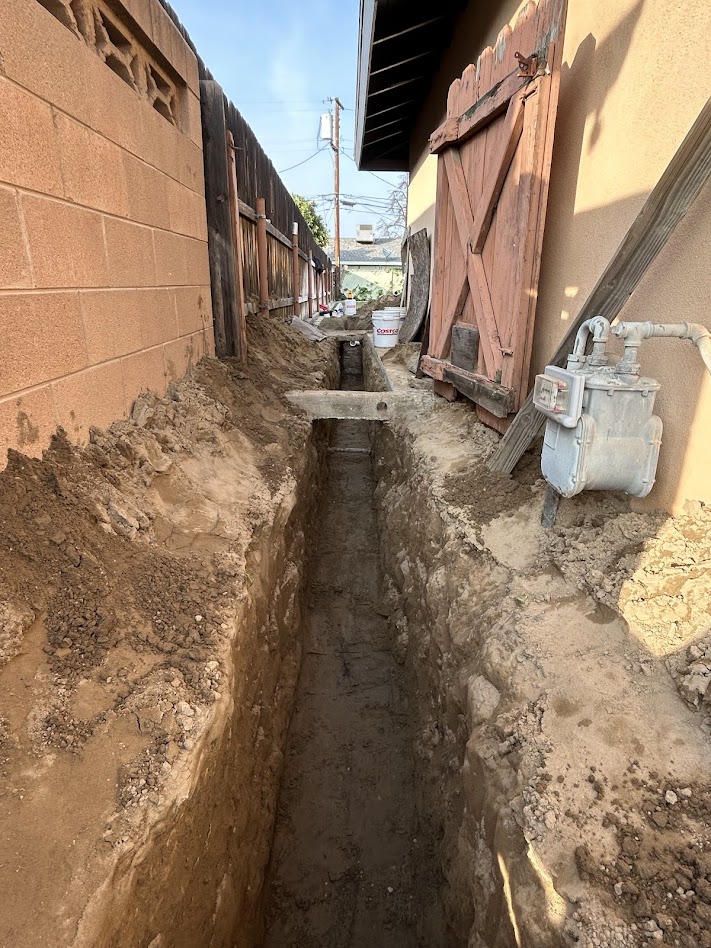 Deep narrow trench excavated alongside a residential house in Bakersfield for a professional sewer line replacement and backyard drainage project by KPS Plumbing.