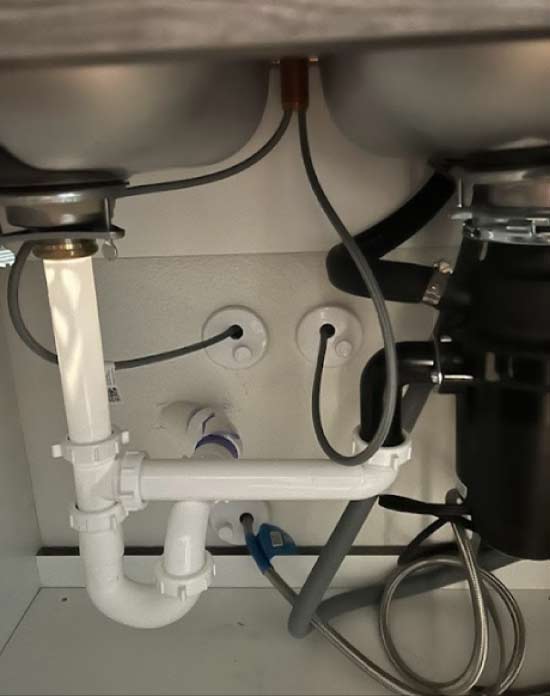 A detailed look at a professional kitchen sink drainage system including a heavy-duty garbage disposal and impeccably routed PVC piping for leak-free performance by the top plumber in arvin, ca