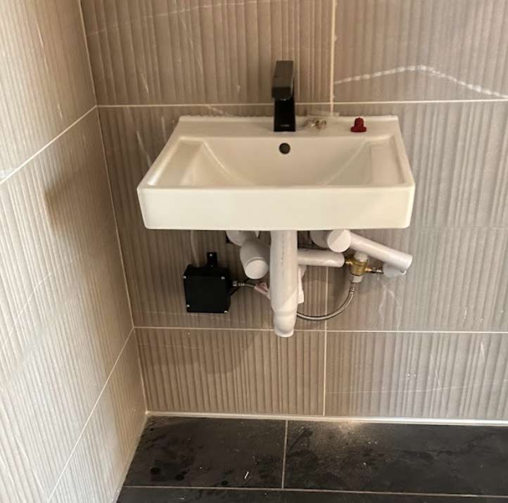 Professional wall-mounted sink fixture installation featuring precision plumbing and expert drain assembly for a modern commercial or residential bathroom remodel.