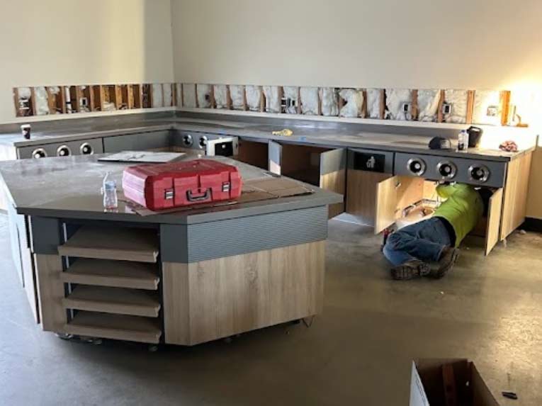 A dedicated plumber in shafter, ca,  performing a complex under-sink installation for a commercial-grade kitchen, ensuring every connection is secure within a modern, organized workspace.