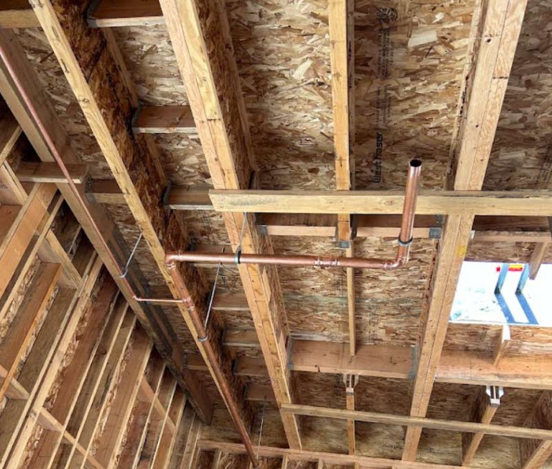 Professional copper pipe installation for new construction plumbing showcasing clean, precise routing through a high-quality wood frame residential ceiling.